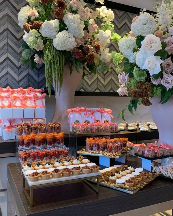 Mesa de postres con flores rosa coral y mostachones individuales en salón moderno